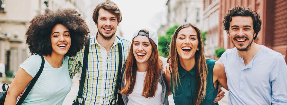 multicultural group of young men and women smiling with arms around each other outside in city