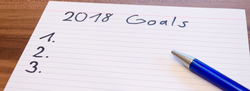 Lined white notecard titled 2018 Goals and numbered one, two, and three with a blue pen on top.