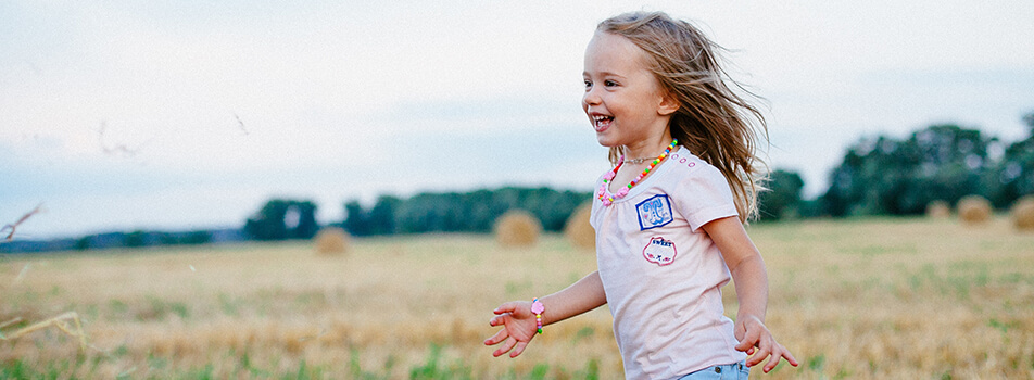 Young child with blonde hair running in the field happy