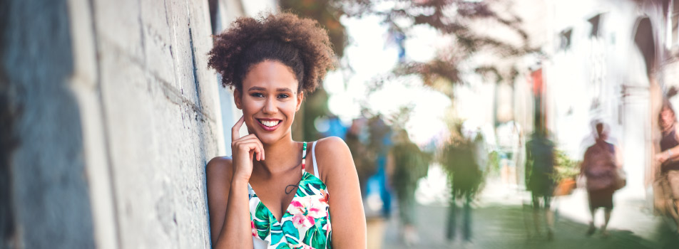 Curly haired woman wears a floral sundress and smiles with her dental crowns