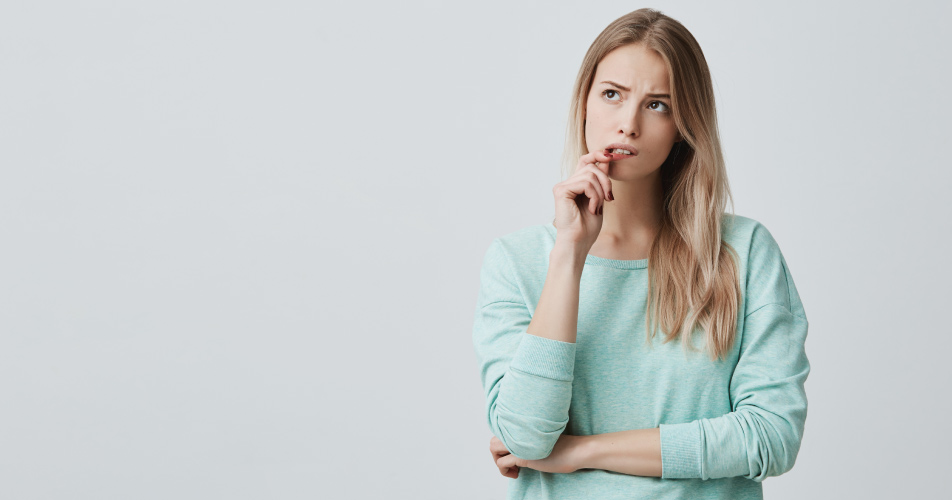 Blonde woman in a mint shirt bites her lip and wonders how to cope with dental anxiety