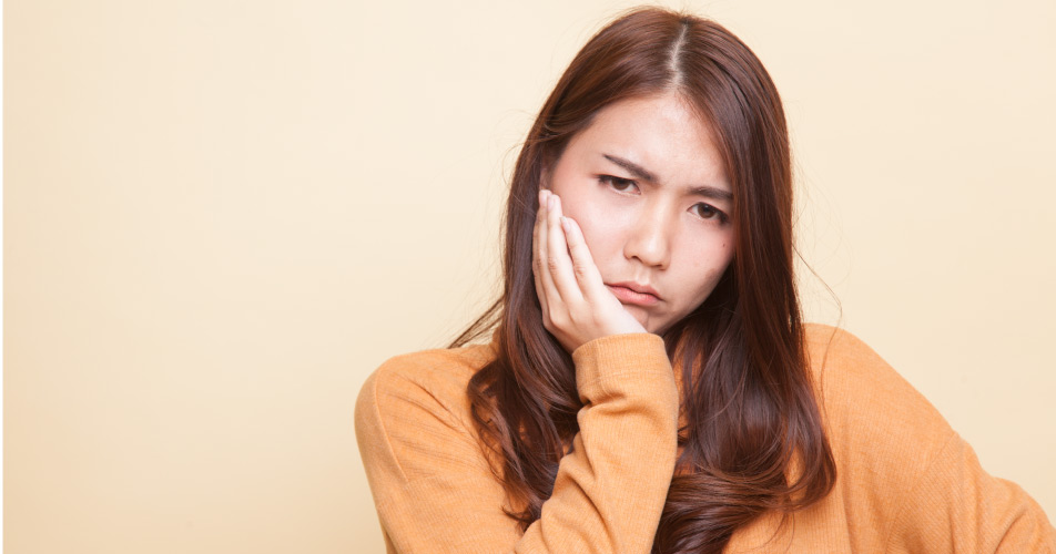 Brunette woman in a yellow shirt cringes in pain due to a toothache from a sinus infection