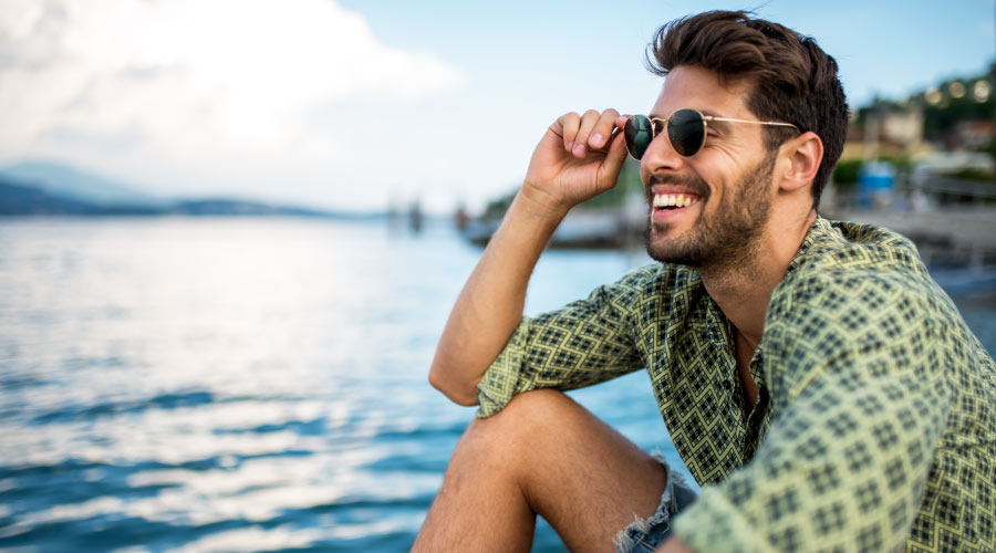 Brunette man wearing a green shirt and sunglasses smiles by the lake with healthier gums in Austin, TX