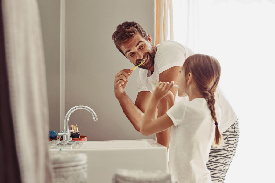 Daddy and daughter brush their teeth together in the bathroom to make brushing fun