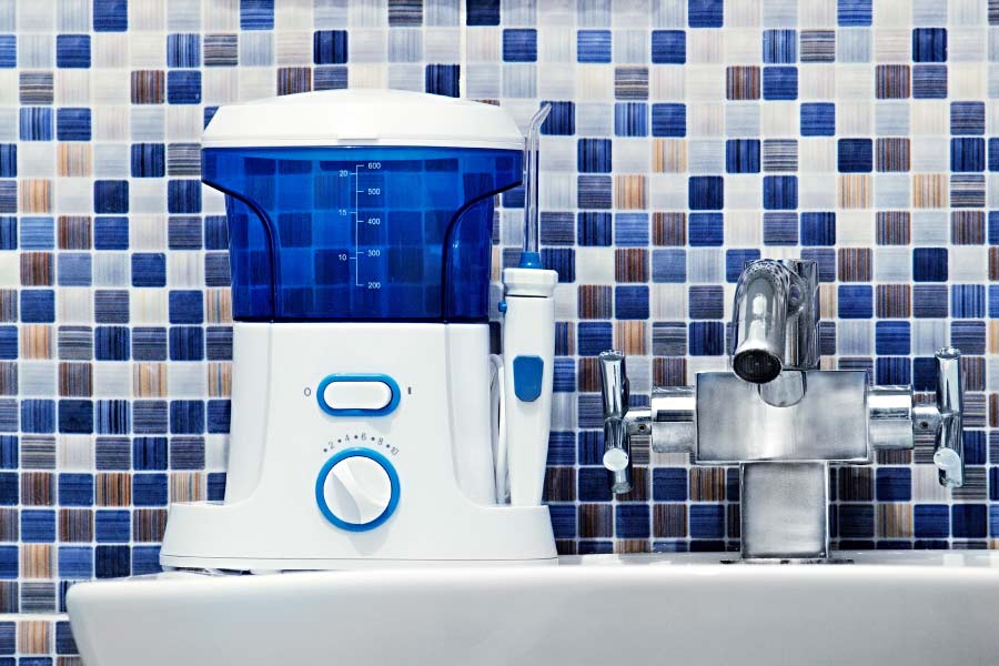 A blue and white water flosser sits on the bathroom counter against an attractive blue and white backsplash