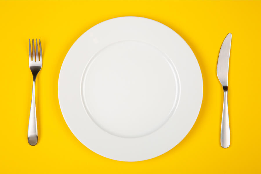 Aerial view of an empty plate with a knife and fork on a yellow table that can fit foods that are good for teeth