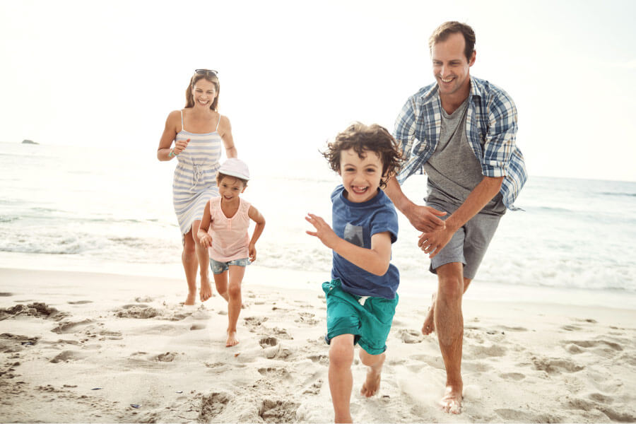 Mom and dad run along a beach with their children, who have great oral health and overall health