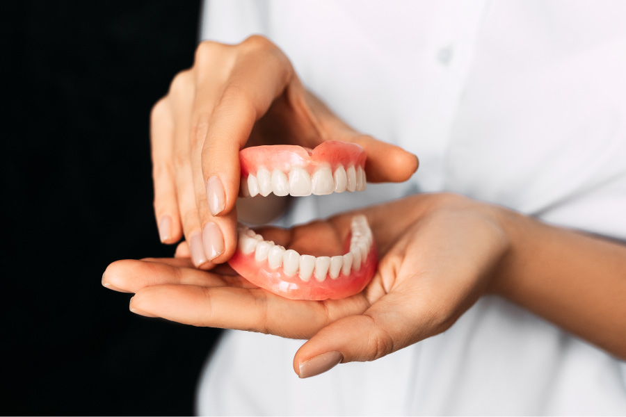 A dentist holds a pair of full dentures in their hands as an affordable tooth replacement in Austin, TX