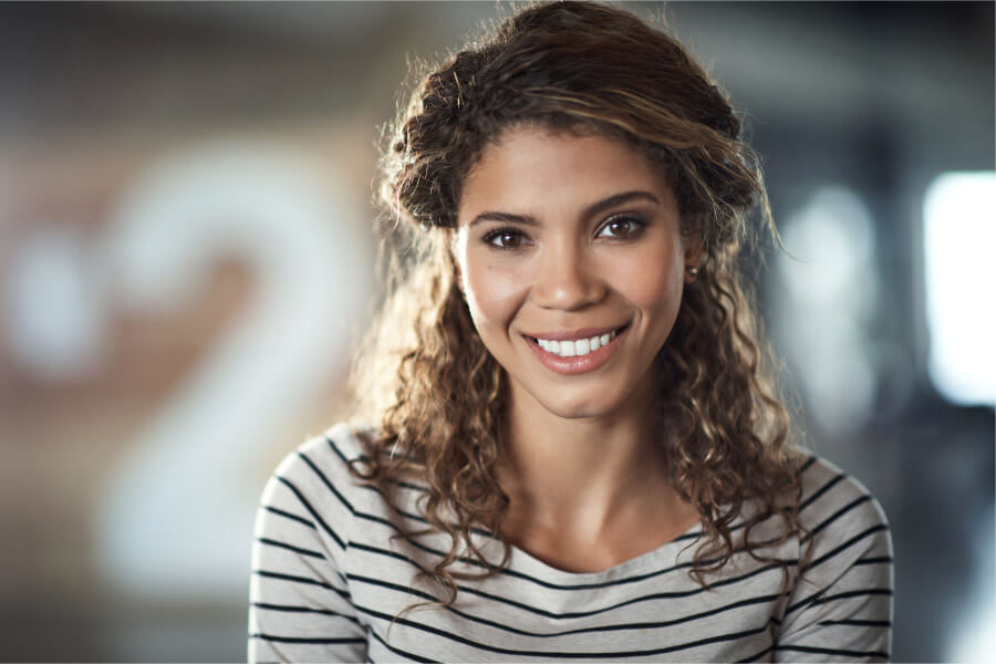 Curly-haired brunette woman in a striped shirt smiles after professional teeth whitening in Austin, TX