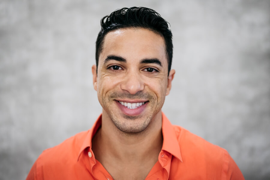 Brunette man in an orange shirt smiles with white teeth because he follows these tips to prevent stains on teeth