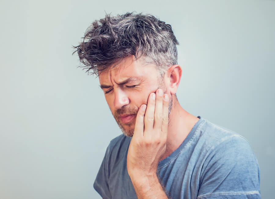 White man with salt and pepper hair cringes in pain and touches his cheek due to a dental abscess