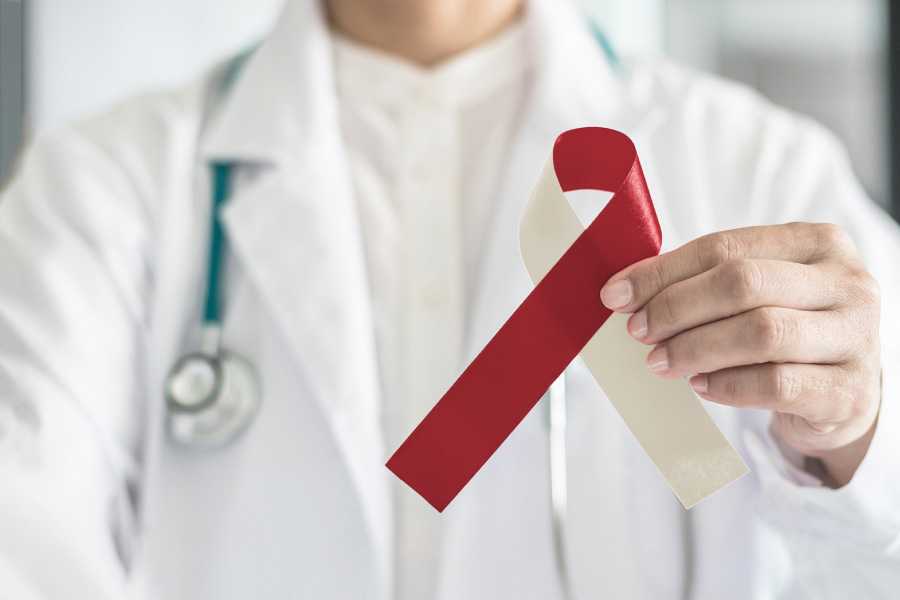 Dentist in a white jacket holds up a beige and red ribbon to represent oral cancer