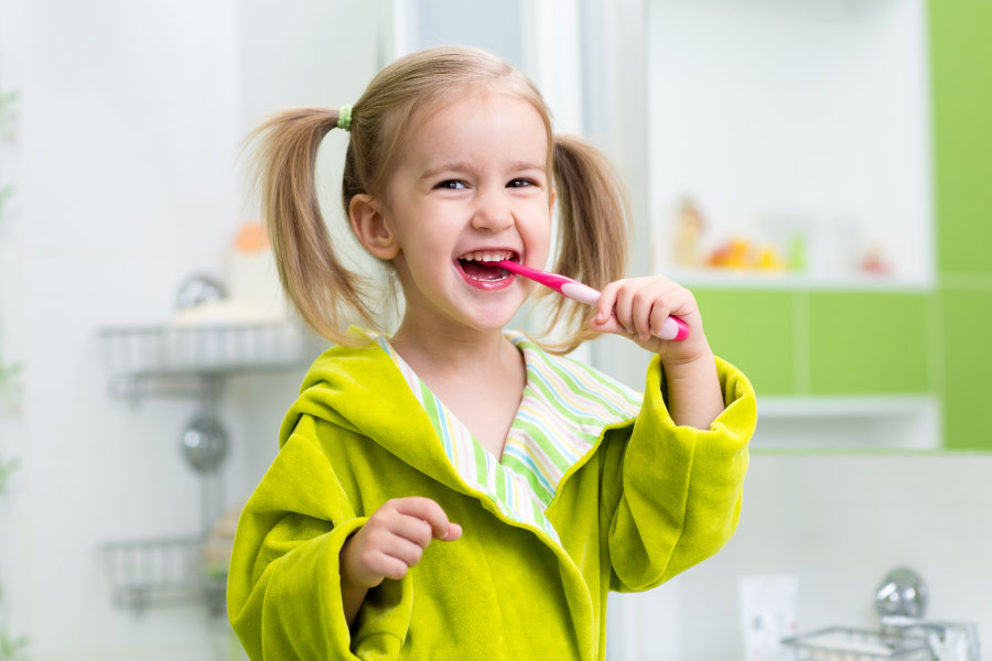 Blond girls with pigtails and a green bathrobe is brushing her teeth.