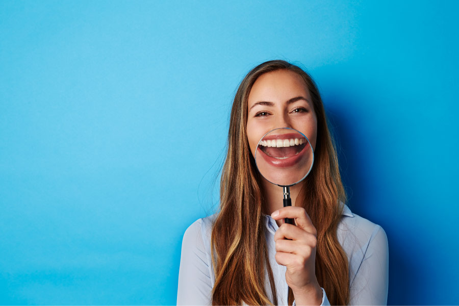 Young woman with long brown hair holding a magnifying glass in front of her smile.