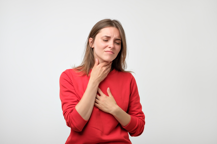 Brunette woman in a red blouse cringes in pain due to heartburn and acid reflux in her throat